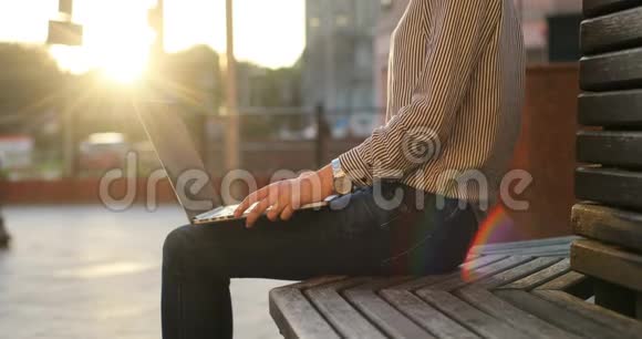 一个穿衬衫的女商人正在长凳上的笔记本电脑上工作晴天街上背景视频的预览图