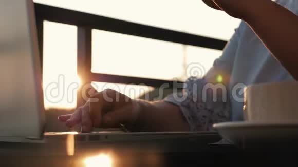 太阳下山时一个女孩正在桌子旁用笔记本电脑和一杯咖啡工作视频的预览图