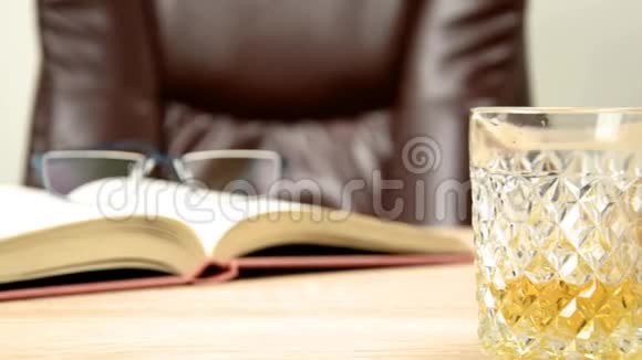 酒精饮料在水晶蜕膜在玻璃里把威士忌倒在背景的木桌上一张椅子上坐下开放书籍视频的预览图
