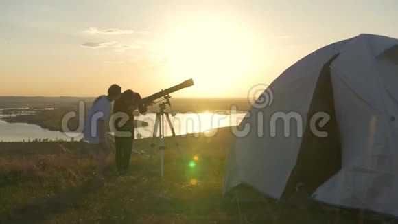 女孩从帐篷里走到朋友们身边透过望远镜看夏天的日落视频的预览图