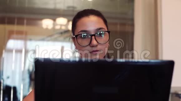 戴眼镜的女商人用电脑和手机工作坐在办公室的桌子上心情很好特写镜头高清视频的预览图