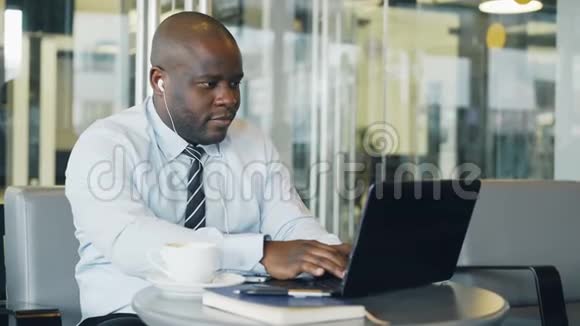 非洲裔美国商人在听音乐时穿着正式服装在笔记本电脑上工作和浏览社交媒体视频的预览图
