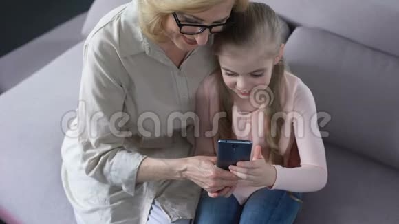 祖母和祖母手里拿着智能手机女孩教奶奶视频的预览图