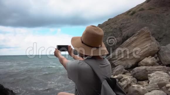 戴帽子的女人在海滩上用手机拍海视频的预览图