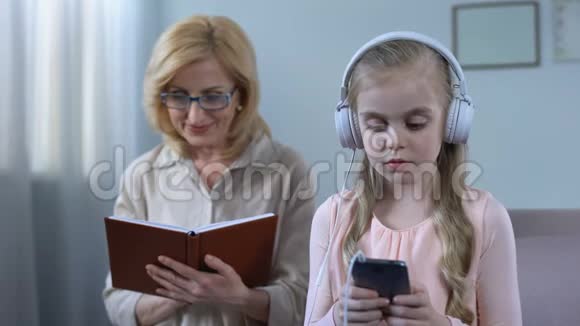 奶奶看书看着小孩听耳机里的有声读物视频的预览图