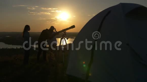 游客帐篷在年轻朋友面前通过望远镜观看夏日日落美景视频的预览图