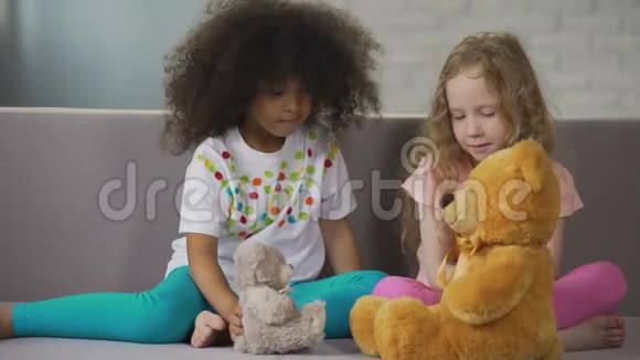 两个多种族的小女孩坐在沙发上玩玩具熊视频的预览图