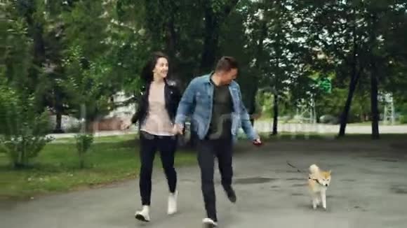 微笑的年轻人夫妻带着可爱的狗在公园里奔跑享受活动手牵着手视频的预览图