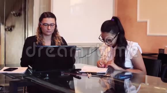 两个穿着商务服装戴着眼镜的女商人坐在桌子旁讨论一个商务项目视频的预览图