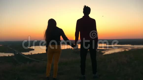 年轻夫妇手牵手在山上看着令人惊叹的日落视频的预览图
