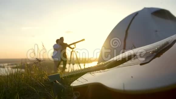 在日落时分年轻夫妇在草地上用望远镜观看吉他视频的预览图