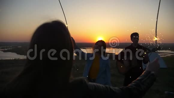 年轻的女人跟着火花舞日落时分在山上弹吉他视频的预览图