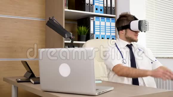 办公室里穿着白色长袍和蓝色领带的年轻医生戴着虚拟现实VR耳机视频的预览图