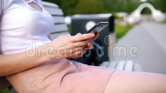 女性的双手在智能手机上写一条信息在户外的长凳上拿一本书视频的预览图