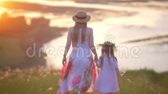 年轻的母亲戴着帽子小女儿牵着手在夏日的夕阳下走下山视频的预览图
