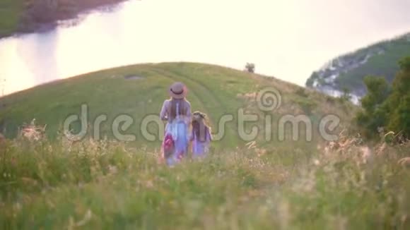 母亲的后景和小女儿一起走下山在夏天的日落时看到河上的景色视频的预览图
