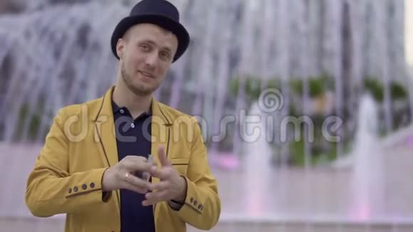 戴着帽子和黄夹克的魔术师巧妙地在手中移动扑克牌视频的预览图