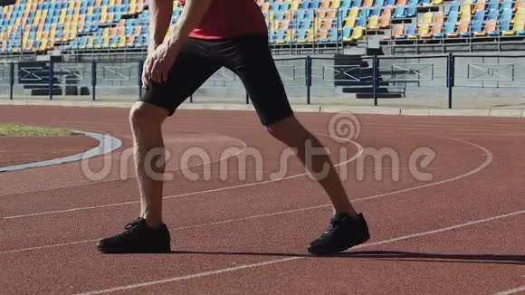 男运动员在慢跑前热身在跑道上伸展双腿视频的预览图