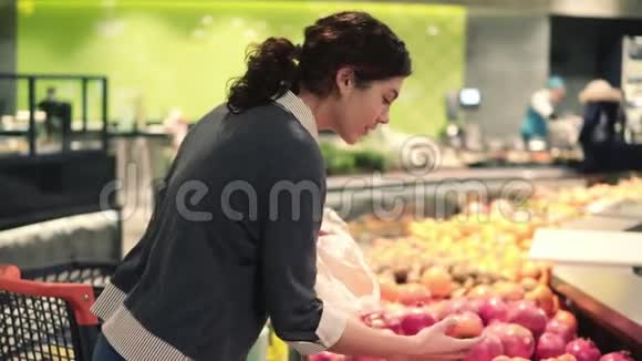 一个年轻漂亮的黑发女孩20正在水果和蔬菜过道里把橘子放进塑料袋里视频的预览图