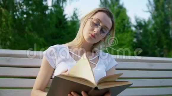 漂亮的女孩在长凳上看书把头发从脸上剪下来视频的预览图
