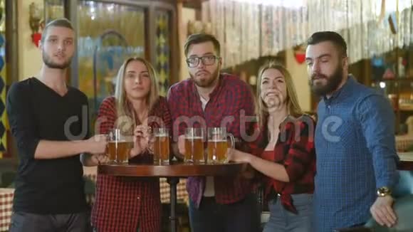 朋友圈年轻人和女孩拿着啤酒杯看着足球在酒吧笑着视频的预览图