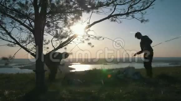 日落时分两个年轻人在山上搭帐篷视频的预览图