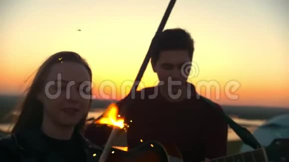 日落时分年轻女子在男友面前和火花匠跳舞在户外弹吉他视频的预览图