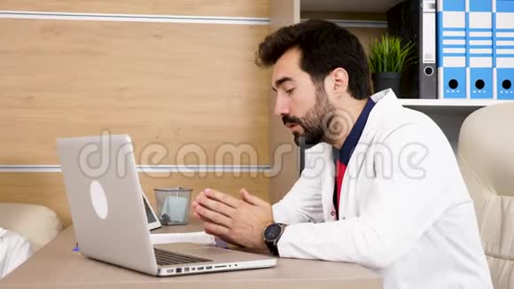 年轻的医生在办公桌前拿着笔记本电脑视频的预览图