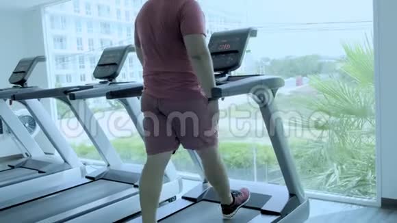 胖乎乎的男人走在跑道上在健身房跑步机上热身视频的预览图