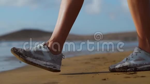 这位女孩穿着运动鞋双脚在沙滩上紧贴大海慢动作稳定视频的预览图