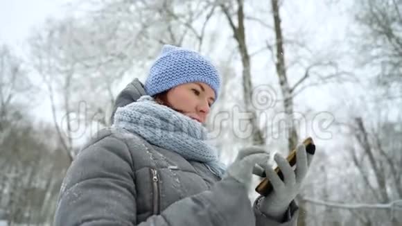 冬季公园的成年女性在电话中阅读信息视频的预览图