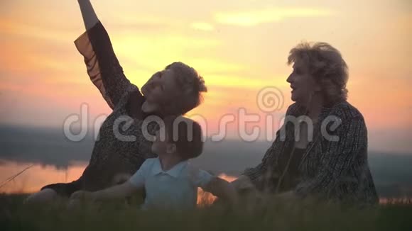 妈妈奶奶和小儿子坐在草地上对着蚊子拍马屁日落时说话视频的预览图