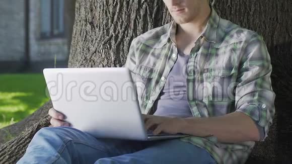 年轻人坐在树下用笔记本电脑大学生在做项目视频的预览图