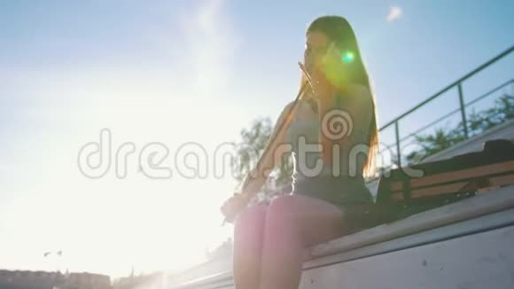 在夏天公园里坐在长椅上靠夕阳拉小提琴的年轻女子视频的预览图
