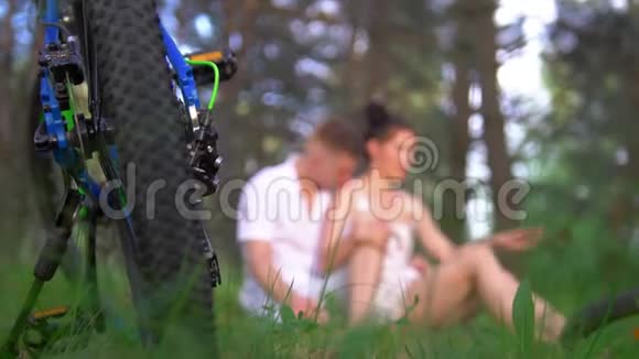 在夏天的森林里骑自行车后年轻夫妇在草地上骑自行车休息视频的预览图