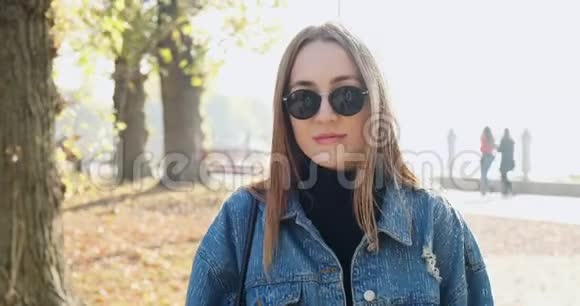 年轻快乐的女孩走在秋天的公园里年轻迷人的女人在阳光下散步微笑视频的预览图