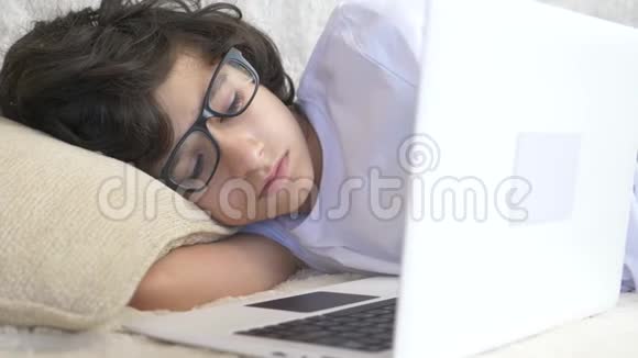 可爱的男孩戴着眼镜睡在笔记本电脑旁边的沙发上4k视频的预览图