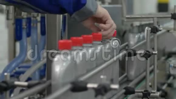 男工在工厂的室内系紧盖子输送线上的一排灰色塑料瓶视频的预览图