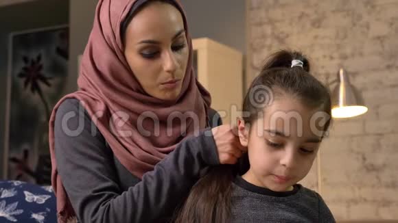 一位年轻的印度母亲戴着头巾给小女儿留了个发型一边说话一边看书视频的预览图