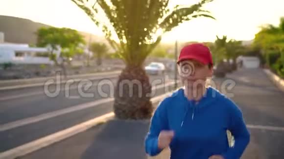 日落时分女人沿着街道在棕榈树之间奔跑健康的生活方式视频的预览图
