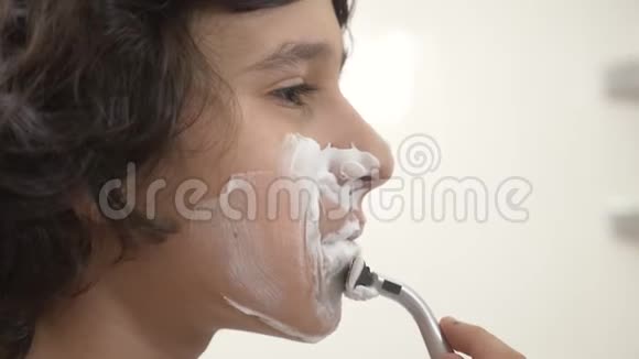 青少年第一次刮胡子十几岁的男孩用剃须泡沫护肤品奶油脸特写视频的预览图