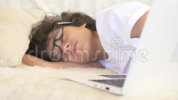 可爱的男孩戴着眼镜睡在笔记本电脑旁边的沙发上4k视频的预览图