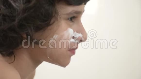 青少年第一次刮胡子十几岁的男孩用剃须泡沫护肤品奶油脸特写视频的预览图