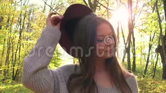 一个戴着帽子的美丽微笑的女孩的肖像在秋天的森林中前景是一片黄色的枫叶慢慢视频的预览图