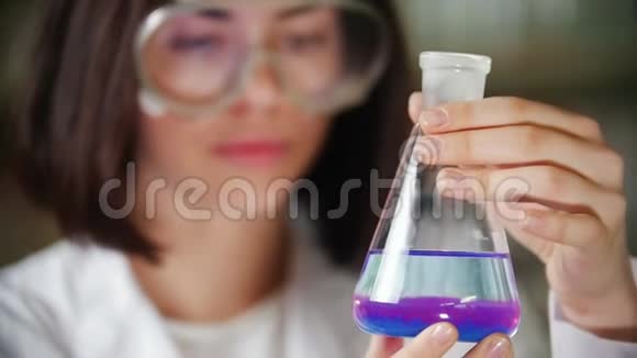 化学实验室的年轻女子拿着一个装有蓝色和紫色液体的瓶子把注意力集中在烧瓶上视频的预览图