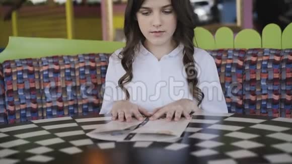 漂亮的微笑的年轻的女孩在咖啡馆里惊奇地看着菜单4K视频的预览图