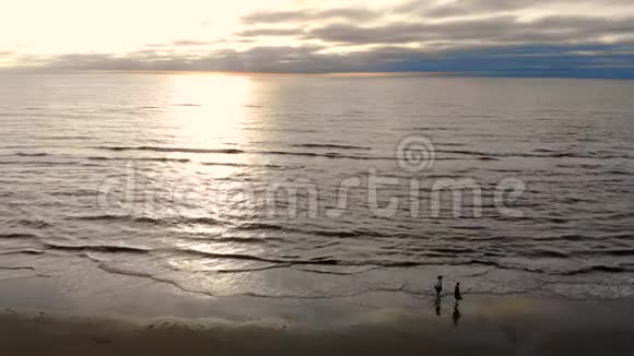 两个人在海滩上散步在阳光明媚的日子飞越大海西方的太阳反射在水中视频的预览图
