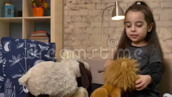 一个小女孩坐在沙发上玩着一只玩具熊和一只狮子梳理着一只玩具狮子的皮毛在家里感到安慰视频的预览图