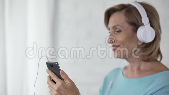 戴着耳机听手机唱歌跳舞的女性退休人员视频的预览图