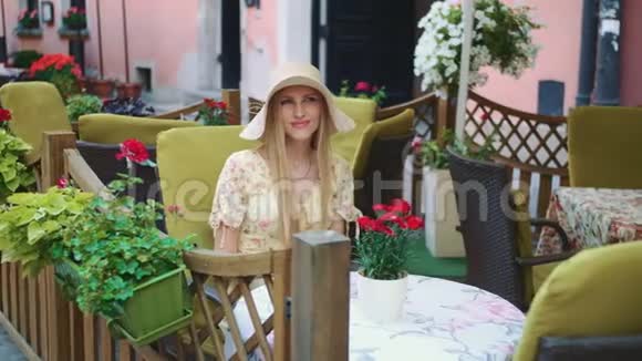 在外面餐馆里微笑的女人在舒适的街道上坐在外面餐馆里的一位开朗的年轻女人视频的预览图